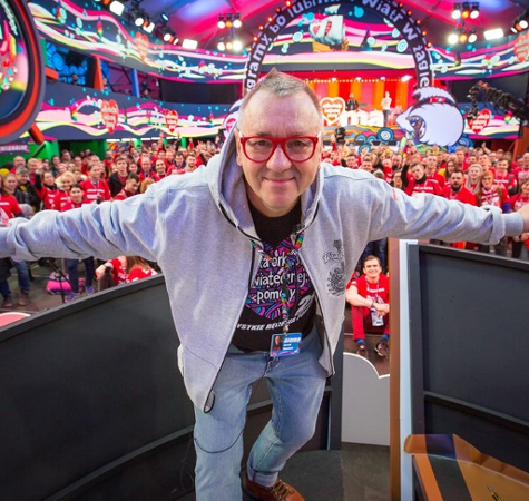 28th Finale of Grand Orchestra of Christmas Charity, photo: Lucyna Lewandowska Colourful photo of Jurek Owsiak - creator of Grand Orchestra of Christmas Charity, taken in a TV studio. In the background people mostly dressed in red t-shirts with Grand Orchestra of Christmas Charity logo.