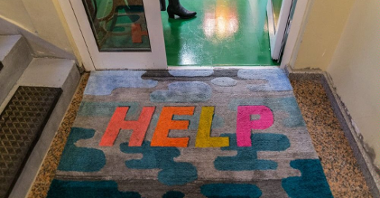 One of the artist's works - a colourful doormat with an inscription "Help" on it in front of the door.