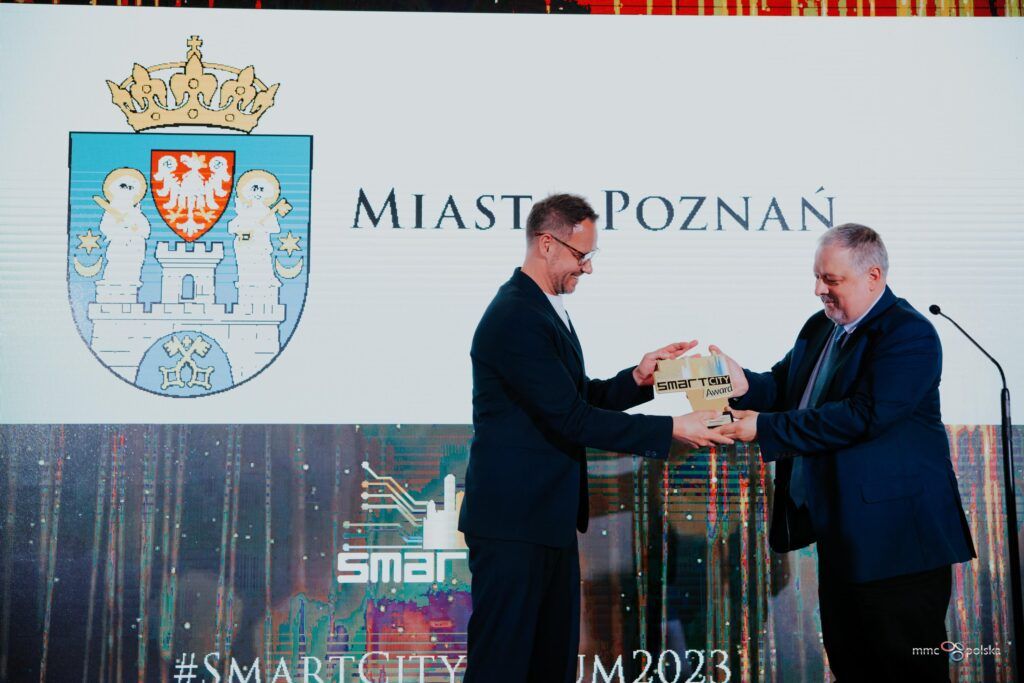 The photo shows two men. One is handing an award to the other. - grafika artykułu