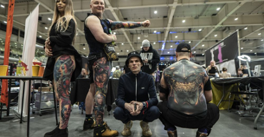Four tattooed people pose for a photo in a large, spacious hall.