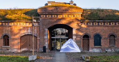 The fort building with a glass entrance gate. In front of the entrance there is a graphic depicting a triangular block of ice with eyes.