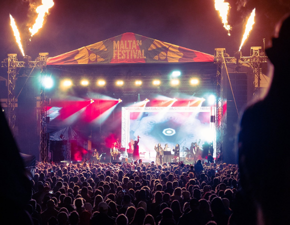 Wyjątkowej atmosferze festiwalu będą towarzyczyć muzyczne wystąpienia artystów z całego świata. Nocna scena plenerowa z dużym tłumem ludzi przed podświetloną estradą oznaczoną banerem "Malta Festival". Na scenie występuje grupa artystów, a po bokach wystrzeliwują płomienie w górę, tworząc efektowną oprawę wizualną.