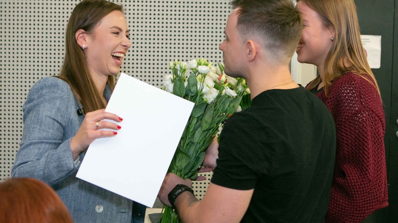 Moment wręczenia podziękowania za prelekcję oraz kwiatów jednej z prelegentek podczas konferencji pod nazwą "Twój czas na zmianę: od inspiracji do działania". Widać radość na twarzy prelegentki.