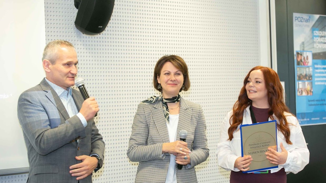 Zastępca Prezydenta Miasta Poznania Jędrzej Solarski przemawia przez mikrofon, obok Dyrektor Wydziału Działalności Gospodarczej i Rolnictwa Joanna Jajus oraz przedstawicielka fundacji Nejmowirna. W tle na drzwiach wisi plakat promujący Poznań Biznes Partner. Wszyscy stoją i otwierają wydarzenie Dzni Przedsiębiorczości Poznań 2024.