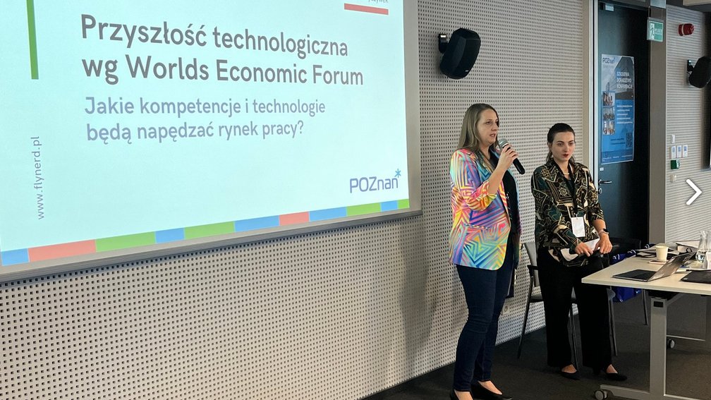 Dwie prelegentki stoją na tle wyświetlanej grafiki promującej prelekcję pod nazwą "Przyszłość technologiczna wg Worlds Economic Formu". Jedna z kobiet mówi przez mikrofon.