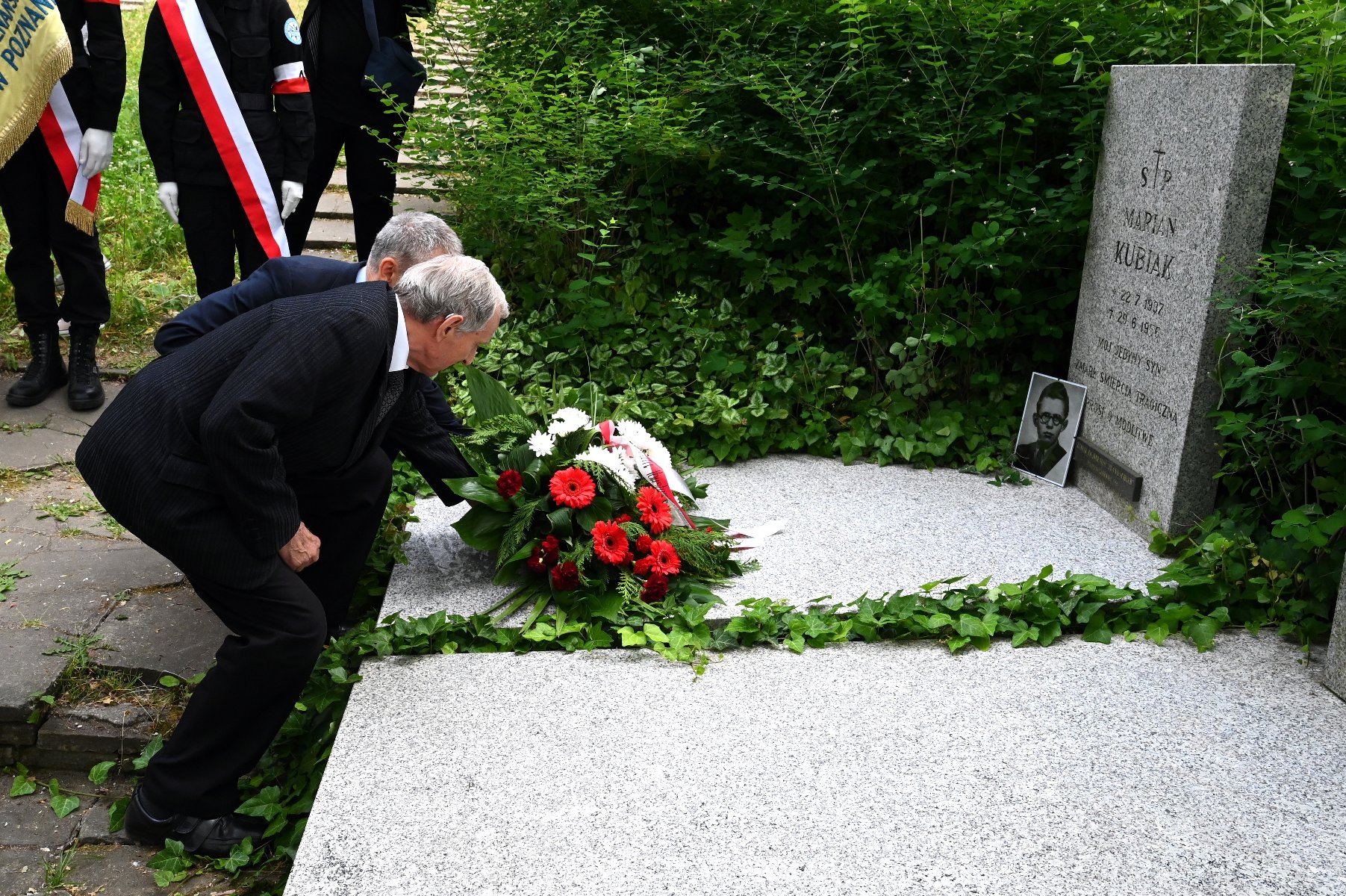 Na zdjęciu dwaj mężczyźni składają kwiaty na grobie - grafika artykułu