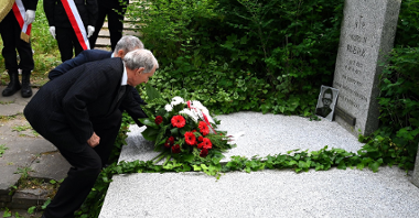 Na zdjęciu dwaj mężczyźni składają kwiaty na grobie