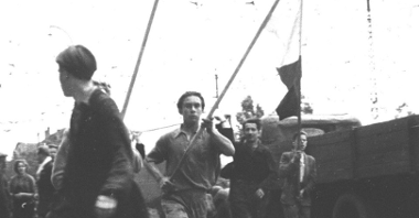 Czarno-biała fotografia strajkujących poznaniaków. W centrum mężczyzna trzyma transparent z napisem "My chcemy chleb dla naszych dzieci"
