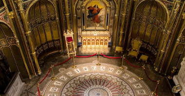 Wnętrze Złotej Kaplicy. Na środku okrągła, zabytkowa posadzka. Posadzka jest otoczona barierkami. W centrum kaplicy znajduje się ołtarz z obrazem, który przedstawia kobiete w czerwonej sukni. Na ścianach znajdują się małe portrety świętych. Wszystkie elementy Kaplicy są złote.