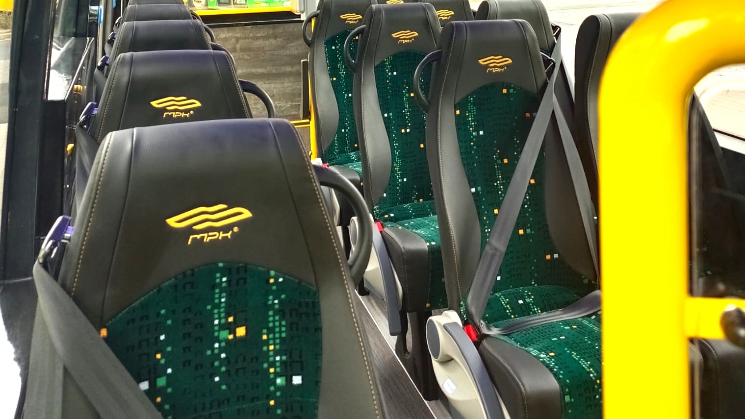 MPK Poznań ogłosiło przetarg na dostawę co najmniej pięciu nowych minibusów fot. Mirosław Nader/MPK Poznań Wnętrze minibusa z rzędami siedzeń. Siedzenia są w czarno-zielone wzory, mają zagłówki i pasy bezpieczeństwa. Na zagłówkach widoczne jest logo MPK Poznań.