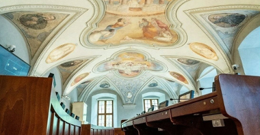 Sala sesyjna Rady Miasta Poznania, pusta, widoczne stanowiska radnych i zdobiące sufit zabytkowe freski