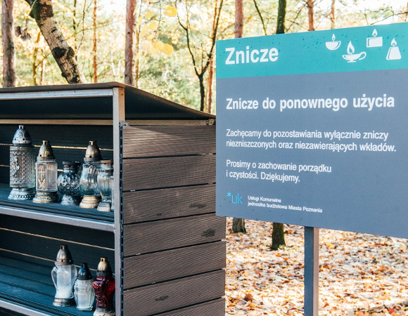 altanka na cmentarzu w niej ustawione znicze obok tablica z informacją, że są to znicze do ponownego wykorzystania