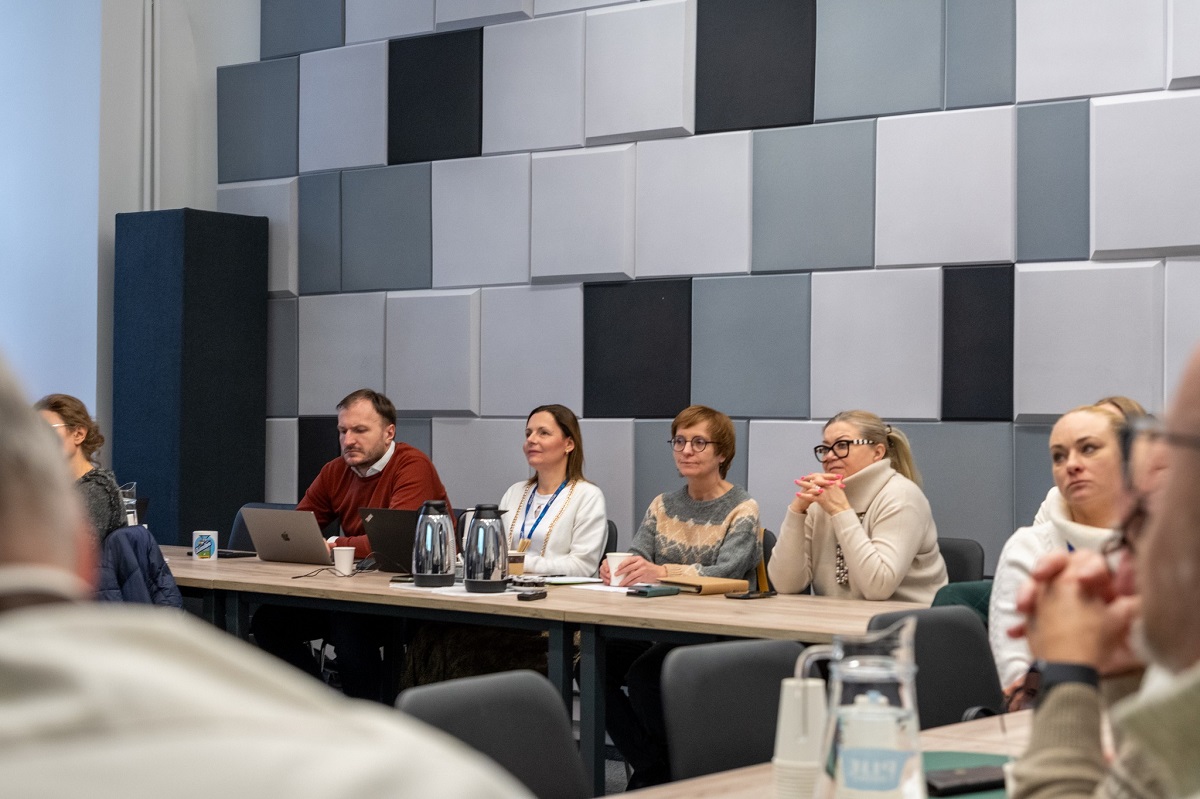 cztery osoby siedzą na stołem prezydialnym w sali konferencyjnej podczas spotkania