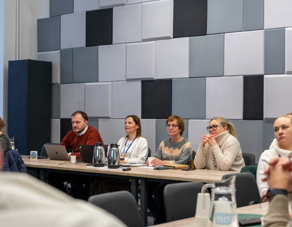 cztery osoby siedzą na stołem prezydialnym w sali konferencyjnej podczas spotkania