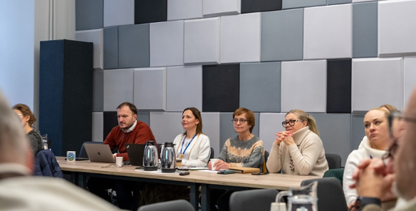 cztery osoby siedzą na stołem prezydialnym w sali konferencyjnej podczas spotkania