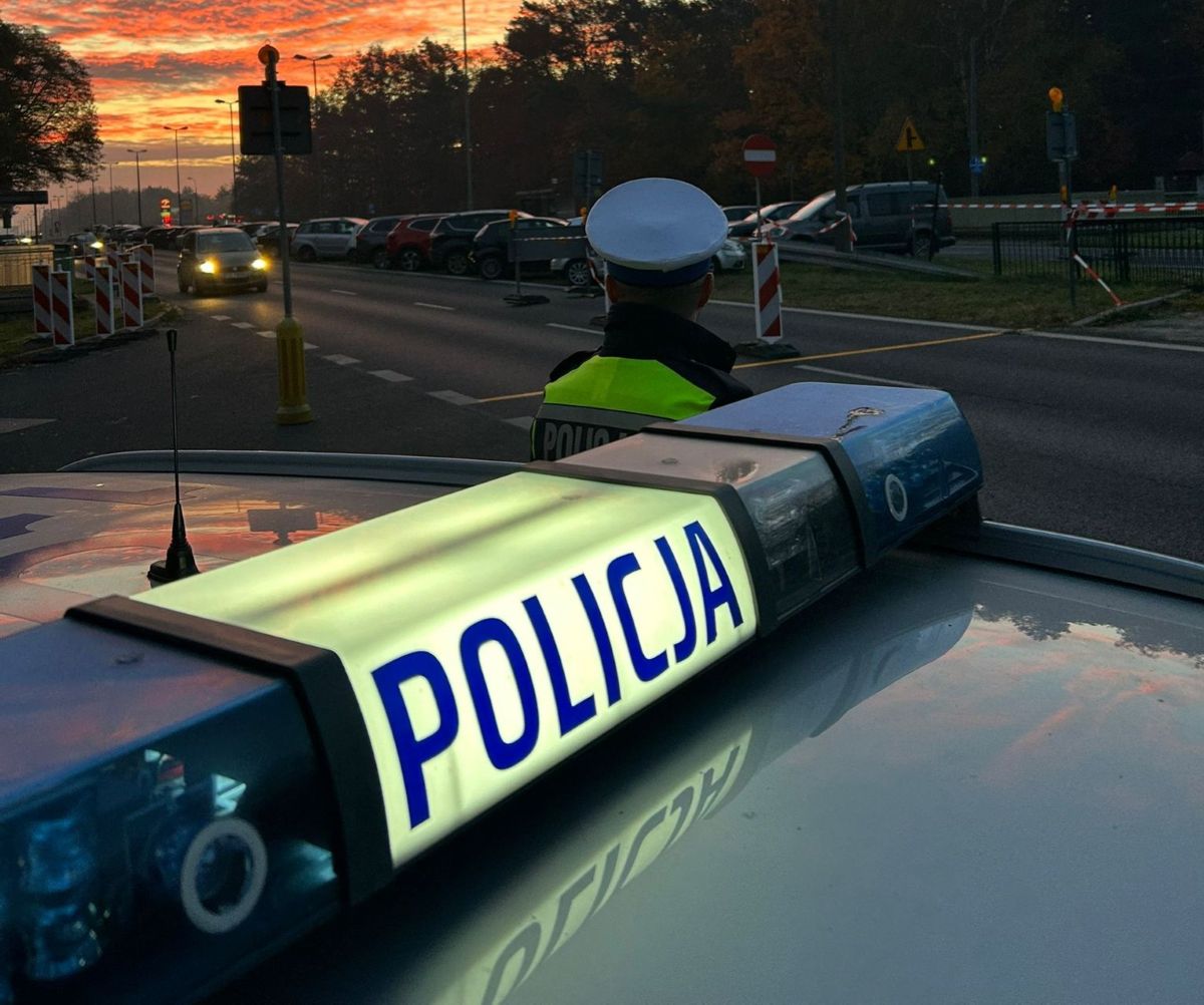 fragment radiowozu policyjnego i policjant przed nim na ulicy