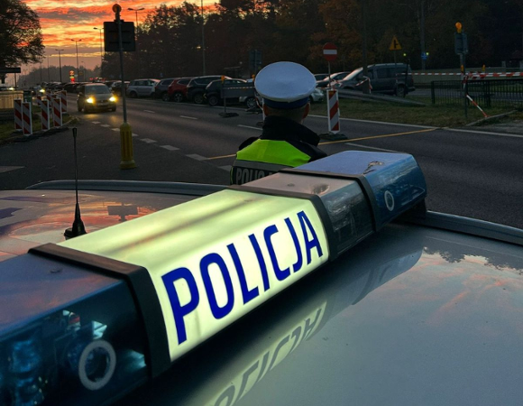 fragment radiowozu policyjnego i policjant przed nim na ulicy