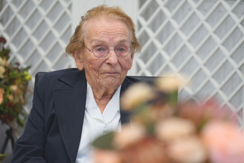 kobiera w podeszłym wieku, w okularach, uśmiecha się lekko, ubrana w ciemną marynarkę i jasną koszulę