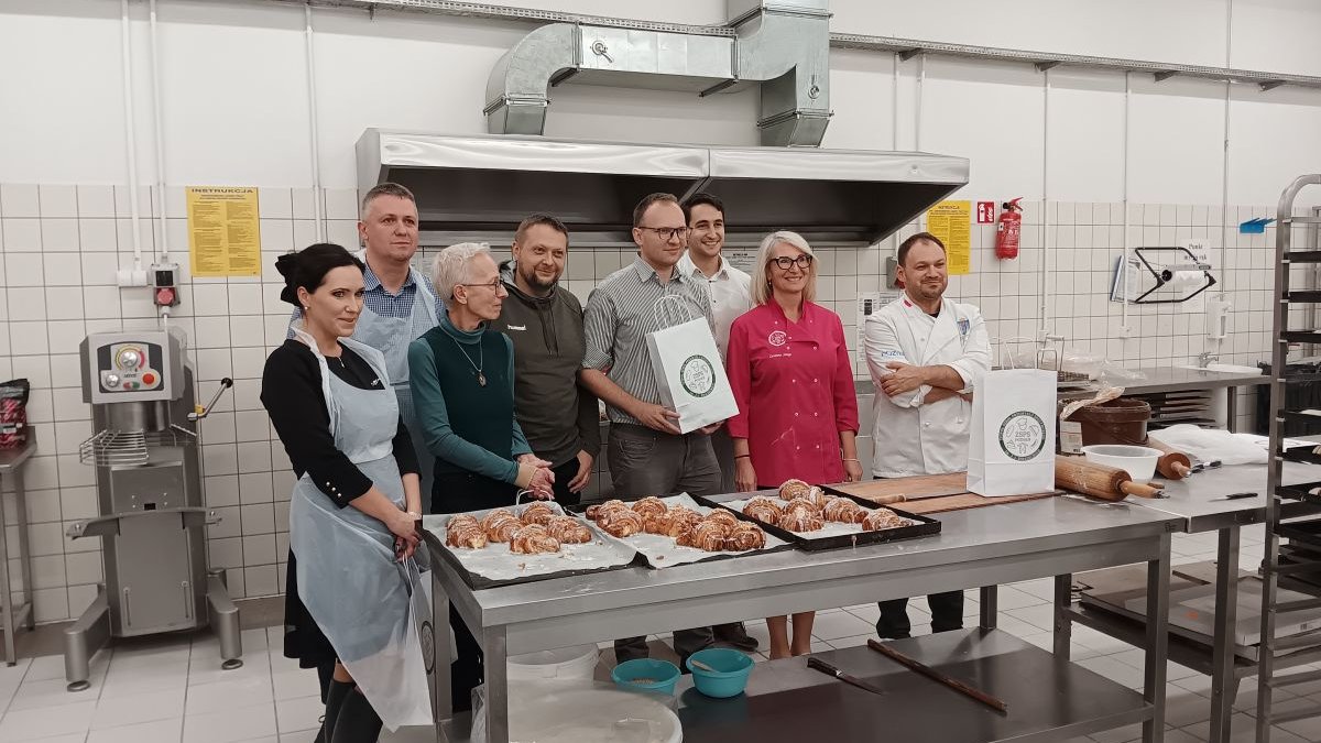 Grupa kilku osób kobiet i mężczyzn w sali piekarniczej przy stole z Rogalami Świętomarcińskimi