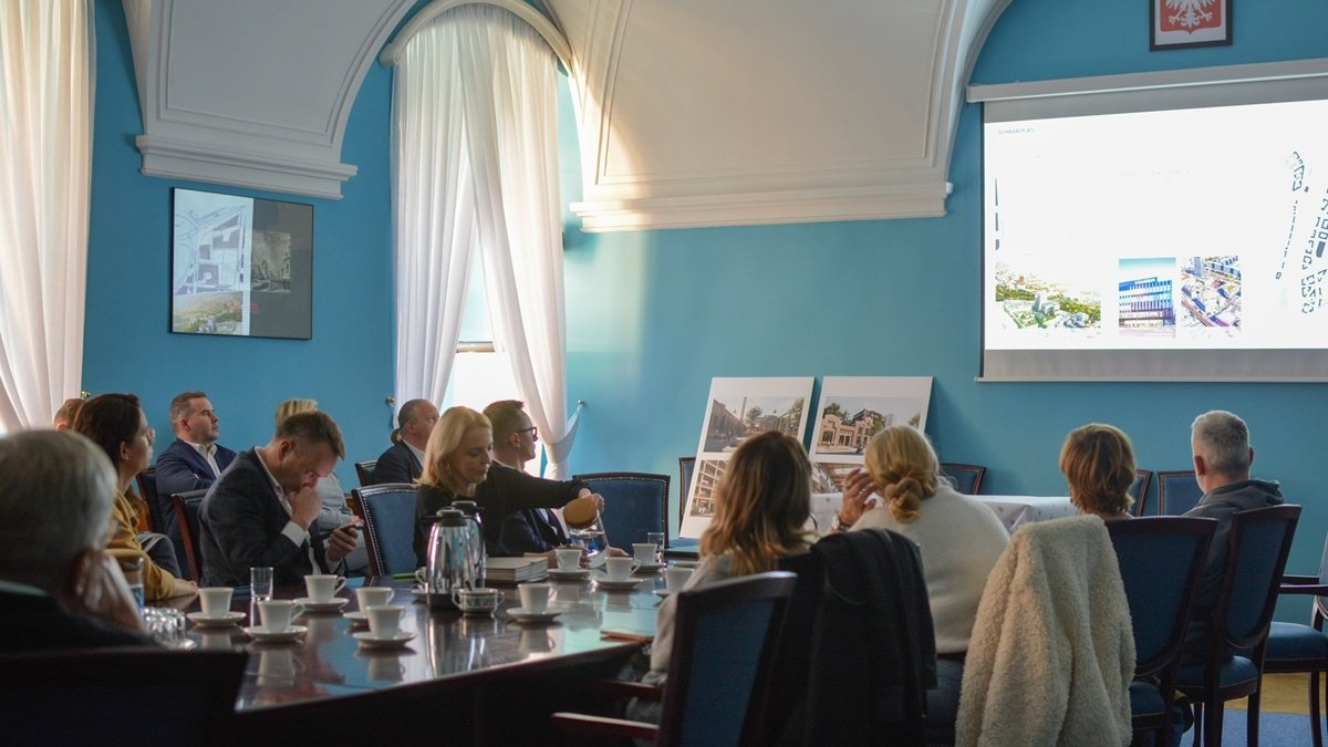 W sali konferencyjnej za stołem siedzi około kilkunastu osób, oglądają prezentację na dużym ekranie