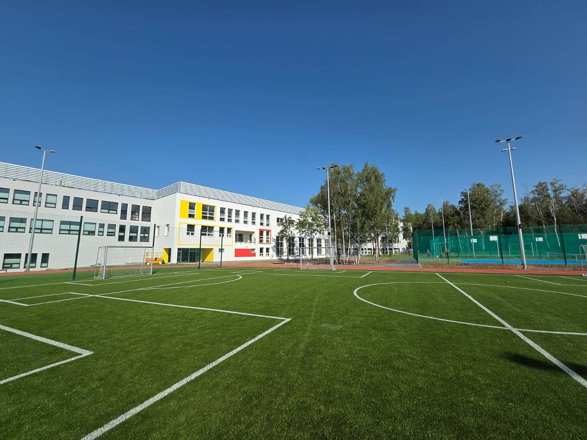 Boisko trawiaste za nim budynek szkolny - grafika artykułu