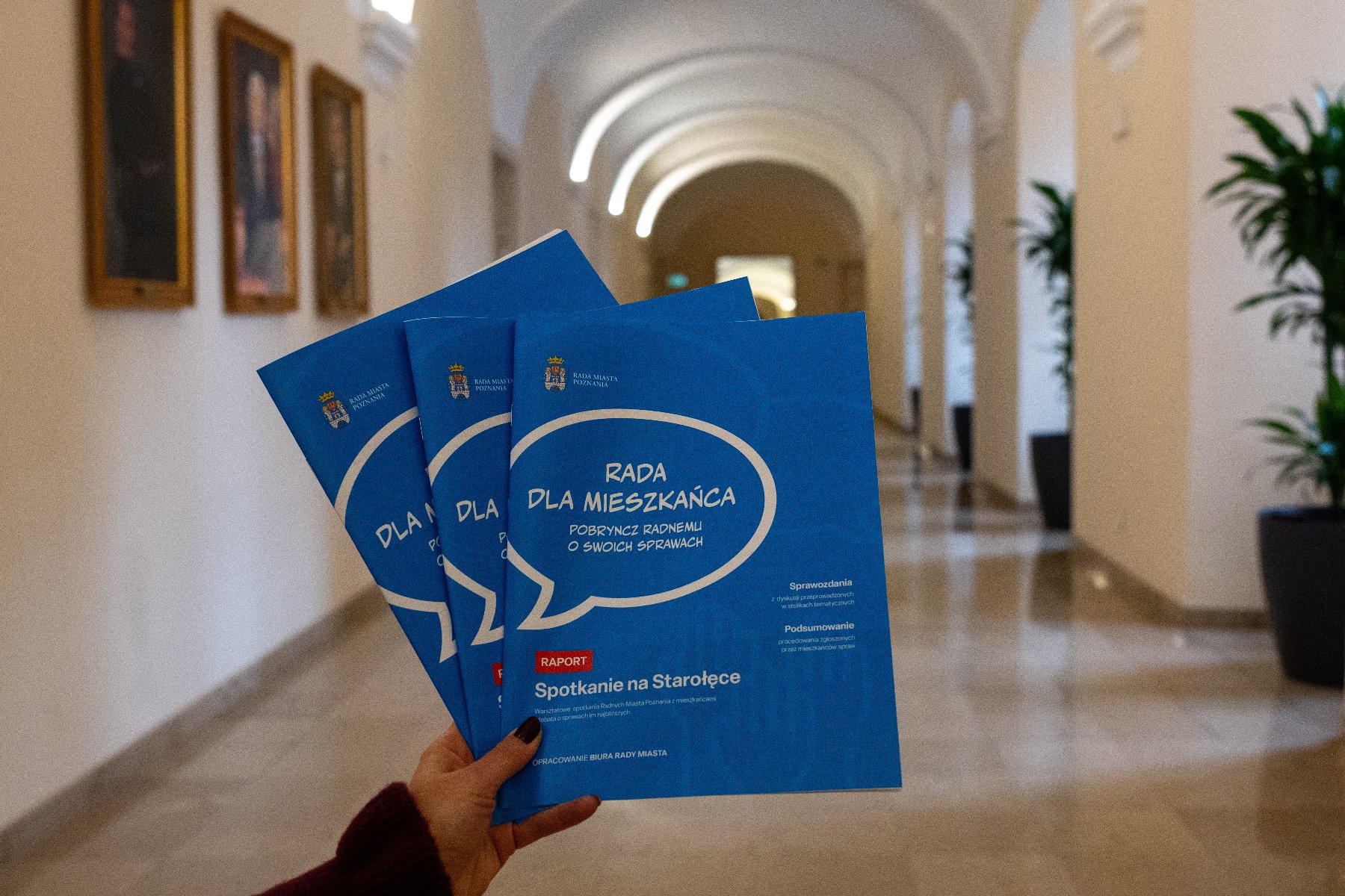 Zdjęcie przedstawia raporty na tle holu. - grafika artykułu