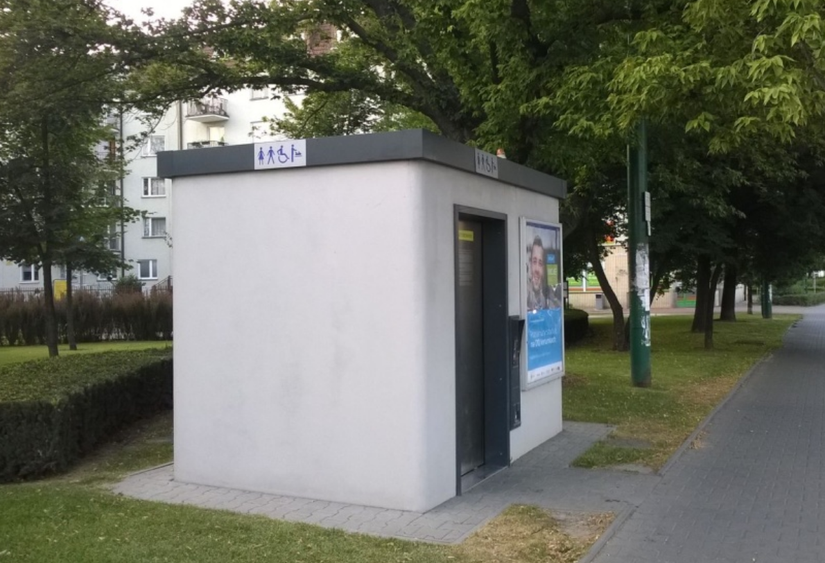 toaleta miejska automatyczna ustawiona przy chodniku obok ulicy z nia skwer - grafika artykułu