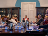 Przy stole konferencyjnym obraduje około kilkanaścioro osób, kobiet i mężczyzn w różnym wieku