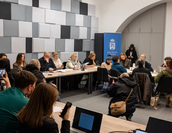 Zdjęcie wykonane w pomieszczeniu. Przy stole w kształcie podkowy siedzą radni i goście posiedzenia.