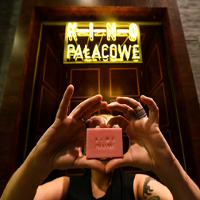 Kobieta trzyma w rękach małe różowe mydło z napisem: Kino Pałacowe. Nie widać jej twarzy. Nad nią neon kinowy.