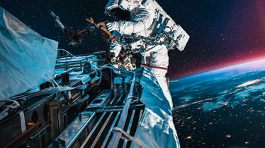 Zdjęcie kosmonauty na zewnątrz statku kosmicznego zawieszonego w gwiezdnej przestrzeni.
