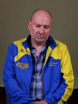 Exhibition poster: photo of a sad looking man in blue and yellow shirt and jacket.