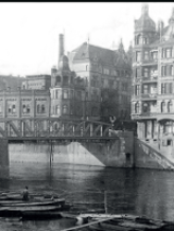 Black and white photo of buildings from past centuries by the river and a bridge.