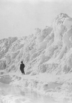 The black-and-white photograph shows a man standing in front of a great snowdrift.