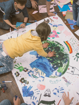 na zdjęciu dzieci malujące na duży papierze