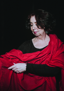 Kobieta w czarno-czerwonym stroju stoi na ciemnym tle.