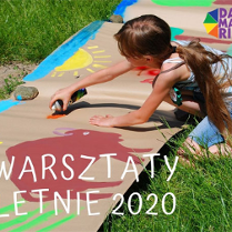 Dziwczyna maluje słońce i zwierzęta na szrym papierze rozłozonym na trawie.