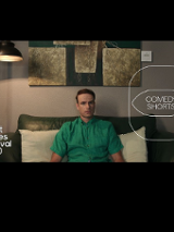 Kadr obrazu na którym widzimy mężczyznę w zielonej koszuli z krótkim rękawem, siedzącego na zielonej dwuosobowej kanapie z dwoma białymi poduszkami za plecami. W tle również lampa stojąca, zaświecona oraz fragment obrazu nad kanapą. Na kadr nałożono logo festiwalu oraz cyklu comedy shorts.