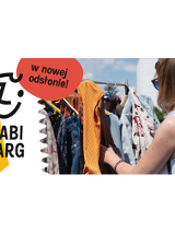 Kobieta przeglada ubrania na wieszaku ustawionym na dworze.Po lewej logo: usmiechnieta twarz, a pod spodem czarny napis na zółto-białym tle.