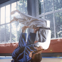 Dwóch zawodników ubranych w białą i niebieską judogę ćwiczy judo.