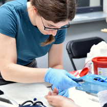 Osoba w rękawiczkach przeprowadza badanie krwi.