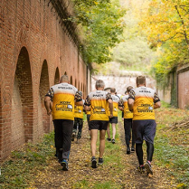 Ludzie w równych zółtych bluzkach biegnący przez leśną ścieżkę w fortyfikacjach z czerwonej cegły.