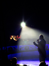 Mężczyzna z mikrofonem stojący na środku namiotu cyrkowego.