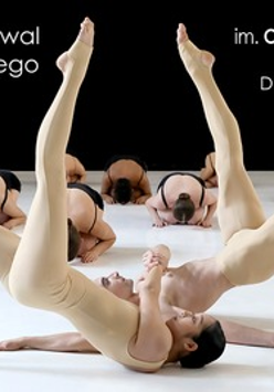 Obraz przedstawia grupę tancerzy występujących na scenie. Na pierwszym planie dwie tancerki znajdują się w efektownej pozie, jedna z nich balansuje na udach drugiej, z nogami wyciągniętymi w górę i splecionymi. Mają na sobie obcisłe, cieliste kostiumy, które zakrywają ich ciała od szyi w dół, sprawiając, że wydają się prawie nadzy i podkreślając linie ich mięśni oraz kształty tworzone przez ich pozy.