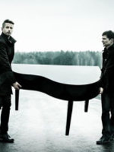 Na czarno-białym zdjęciu dwóch mężczyzn niosących fortepian.