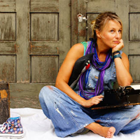 Eliza Piotrowska siedzi po turecku przy drzwiach z maszyna do pisania na kolanach. Obok postawiona walizka do maszyny.
