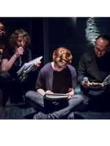 Kilku mężczyzn siedzi na scenie, każdy z nich trzyma przed sobą otwartą książkę. Jeden z mężczyzn patrząc na otwartą książkę czyta do mikrofonu.