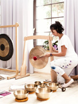 Kobieta gra na misach i gongach, Na podłodze na matach leżą uczestniczka zajęć.