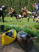 grupa chłopców walczy na trawie, 2 odpoczywa w canoe.