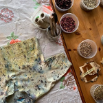 Na stol materiał a na nim koszulka do farbowania. Obok w pojemnikach produktu do robienia naturalnych barwników.